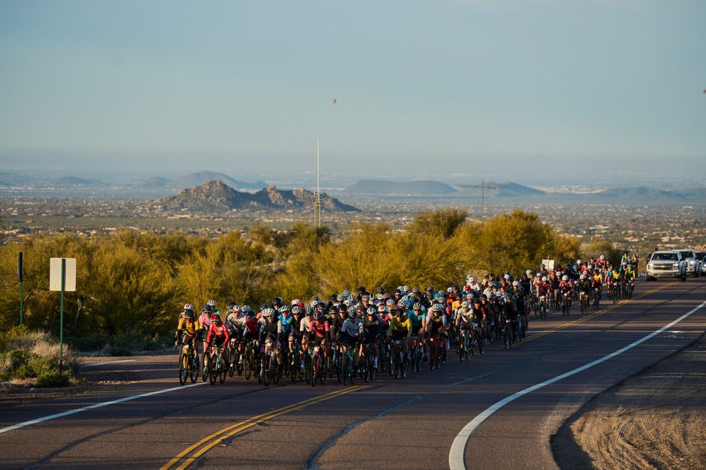 Hundreds of cyclists racing along a highway in the Arizona Desert