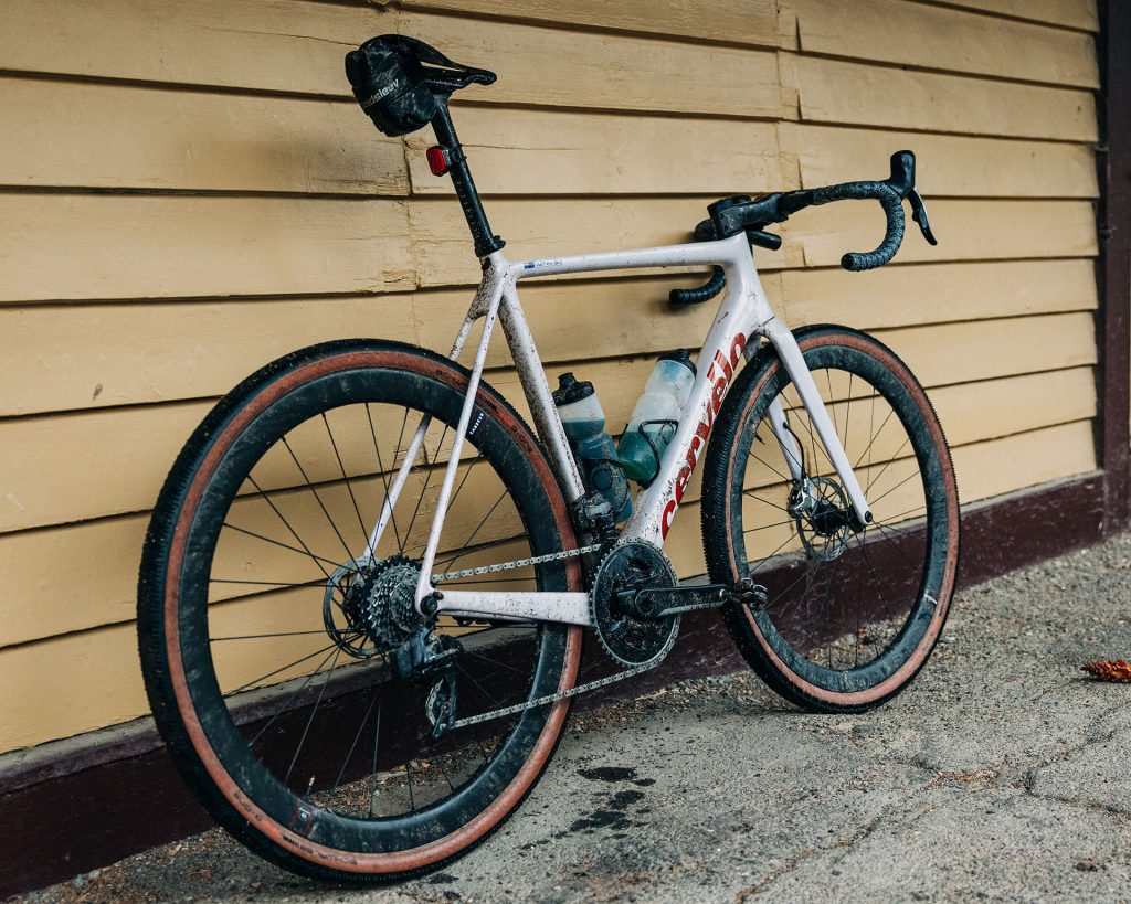 A muddy white Cervelo bike leaning against a yellow weatherboard building.