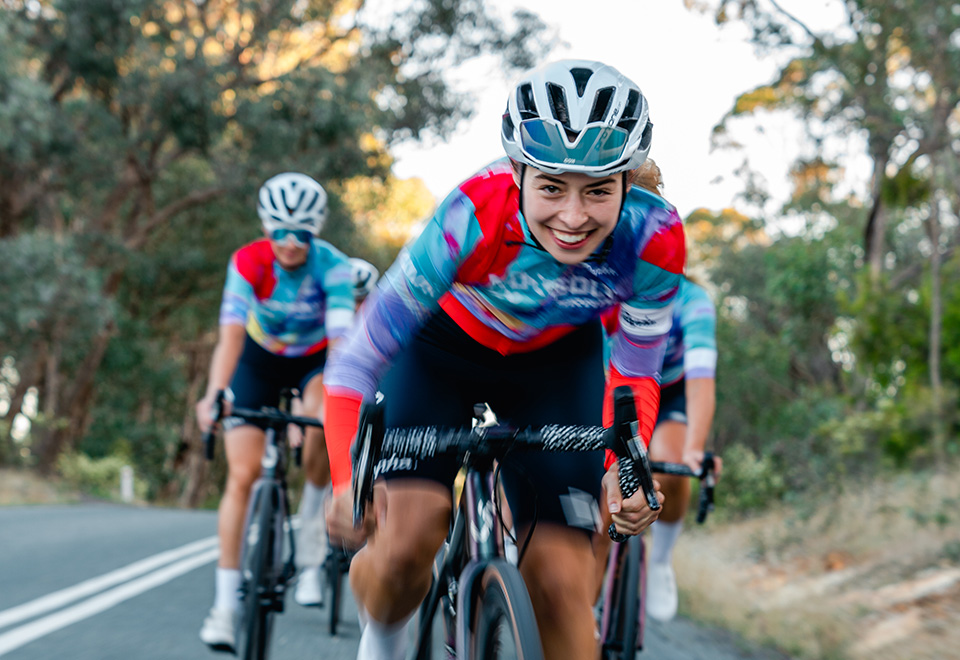 Elizabeth Nuspan rides ahead of a group, in her bright-coloured Roxsolt jersey and a big smile on her face.
