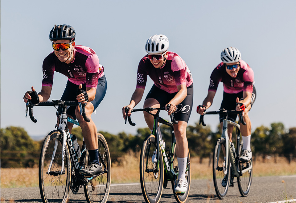 Group of three riders in pink cycling jerseys.